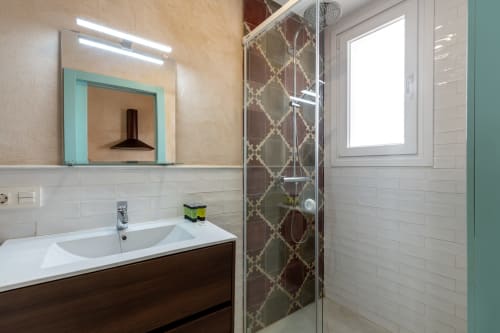 Baño moderno en Apartamento Triana con azulejos blancos, tocador de madera oscura, marco de espejo turquesa y diseño geométrico