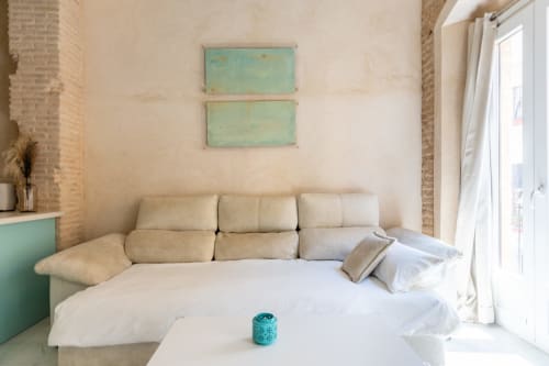 Estudio luminoso en Sevilla con sofá cama color crema, arte mural turquesa y puertas de balcón con vistas a la ciudad