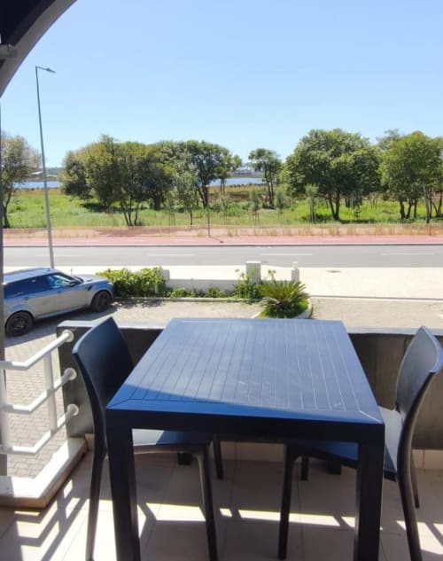 Balcony view at Hotel Slow Stay Esposende with blue table, chairs, riverside park, and trees overlooking water