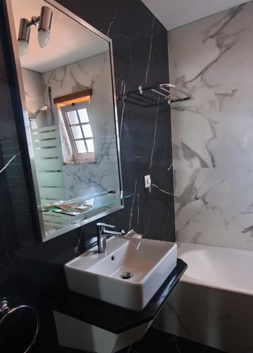 Modern bathroom at Hotel Slow Stay with white sink, marble tiles, illuminated mirror, and shower area in Esposende