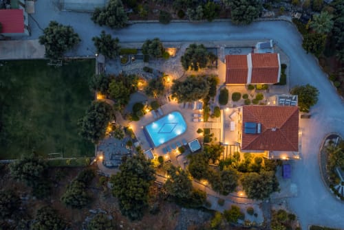 Villa Freedom aerial view at dusk with illuminated pool, red-roofed buildings, and surrounding cypress trees in Kokkino