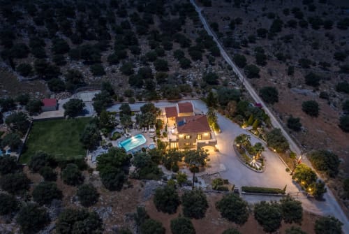 Villa Freedom aerial view at dusk, illuminated Cretan property with pool, landscaped grounds, surrounded by olive trees in