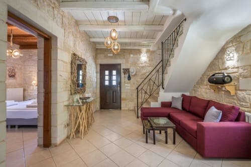 Villa Freedom living area in Kokkino Chorio, Crete with burgundy sofa, stone walls, and staircase