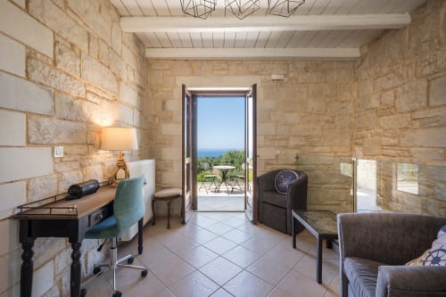Villa Freedom bedroom in Crete with stone walls, desk, seating, and terrace view overlooking sea
