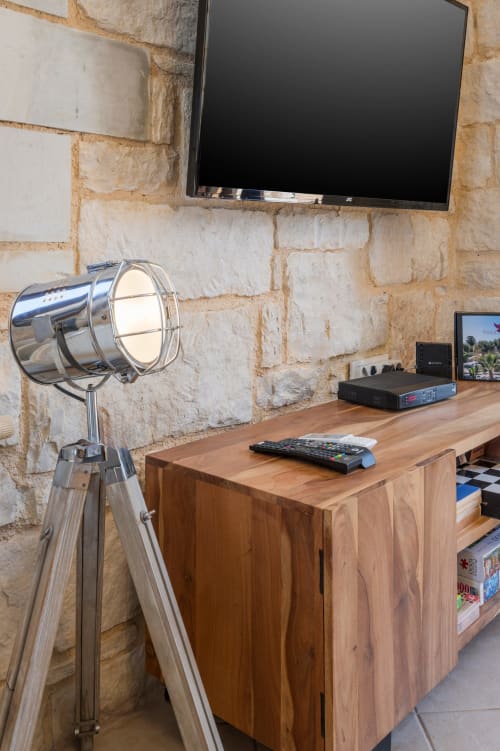 Modern media setup at Villa Freedom with stone wall, flat-screen TV, wooden desk, and tripod lamp in Crete
