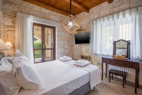 Elegant bedroom at Villa Freedom in Crete with stone walls, wooden ceiling, and modern amenities