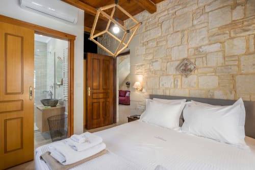 Spacious bedroom at Villa Freedom in Crete with stone walls, wooden beams, king bed, and en-suite bathroom