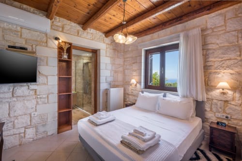 Luxury bedroom at Villa Freedom in Crete with stone walls, wooden ceiling, and sea view from window