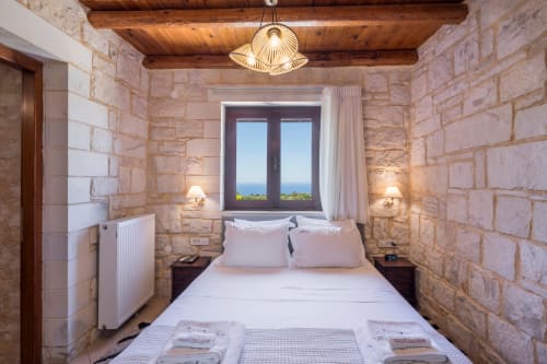Cozy bedroom at Villa Freedom in Crete with stone walls, sea view window, and wooden beams