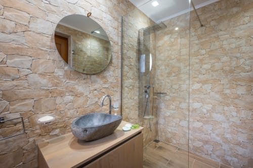 Modern bathroom at Villa Freedom with stone walls, slate sink, round mirror, and glass shower enclosure in Kokkino Chorio,