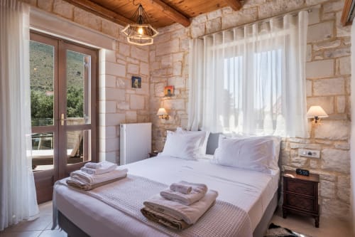 Luxury bedroom at Villa Freedom with stone walls, white linens, and terrace overlooking Kokkino Chorio, Crete