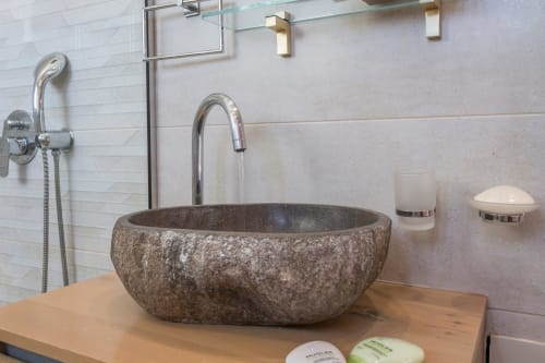 Modern bathroom at Villa Freedom in Crete featuring a rustic stone vessel sink with chrome faucet and amenities.