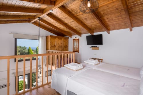 Spacious bedroom at Villa Freedom in Crete with wooden beams, two beds, TV, and balcony overlooking Kokkino Chorio