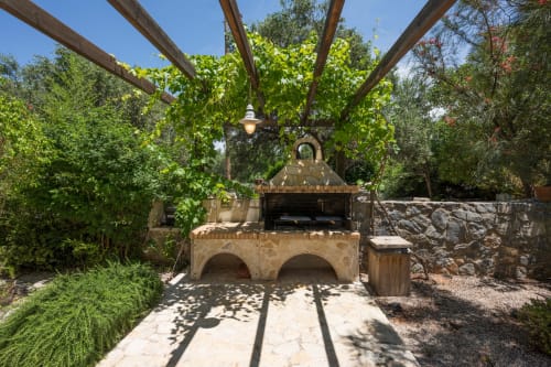 Stone outdoor pizza oven with wooden pergola and lush greenery at Villa Freedom, Kokkino Chorio, Crete