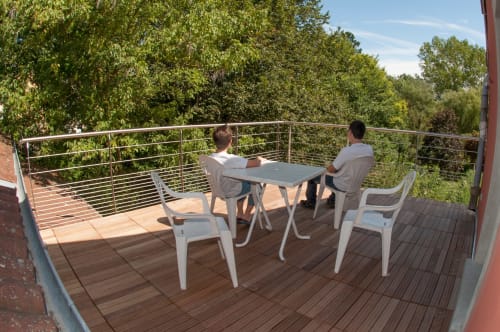 Deux clients savourent des boissons sur une terrasse en bois avec vue sur les jardins luxuriants du Jardin de la Reyssouze, gîte français