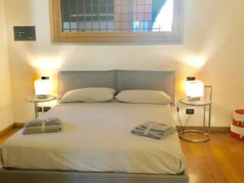 Camera da letto spaziosa con testata grigia, biancheria bianca, lampade da comodino gemelle e pavimenti in legno nella stanza Rosa di Appartamento