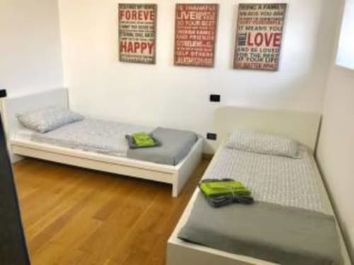 Due letti gemelli con asciugamani verdi nella camera Rosa di Appartamento Franciacorta, arte murale motivazionale sopra, pavimento in legno