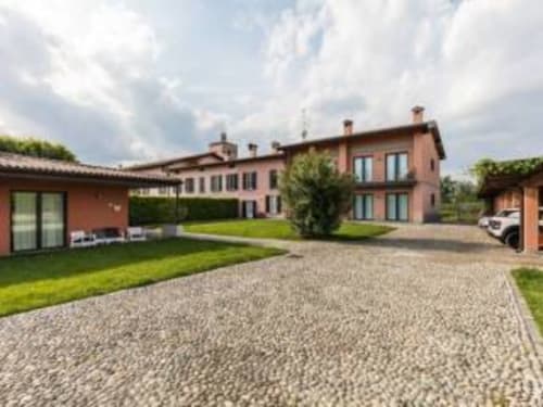 Cortile di Appartamento Franciacorta con edifici in terracotta, prato curato, vialetto in ghiaia e auto parcheggiata a Cazzago San