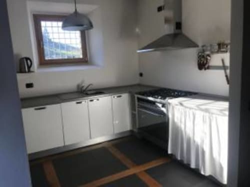 Cucina moderna con armadi bianchi, piano di lavoro scuro, fornello a gas e lampadario sospeso nella camera Rosa dell'Appartamento Franciacorta