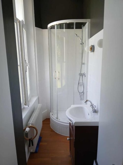 Salle de bain moderne avec douche à paroi vitrée incurvée, lavabo blanc et parquet en bois à la villa du château de Mons Boubert
