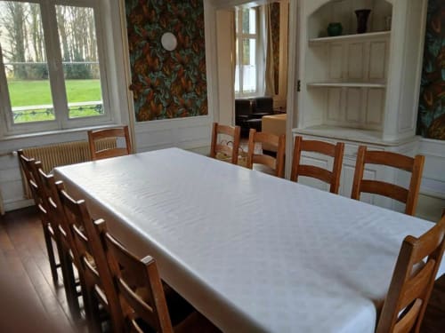 Salle à manger élégante du château de Mons Boubert avec nappes blanches, chaises en bois, vue sur le jardin et papiers peints d'époque
