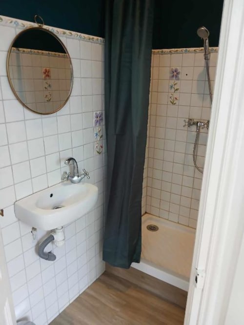 Salle de bains du château de Mons Boubert avec carrelage blanc, carreaux de fleurs décorativement peints, miroir ovale et lavabo blanc