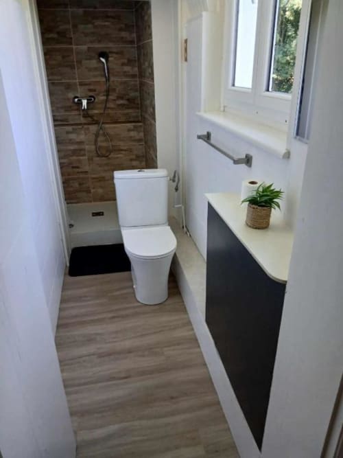 Salle de bain moderne avec toilettes blanches, vanité foncée, douche vitrée et fenêtre à la villa Le château de Mons Boubert