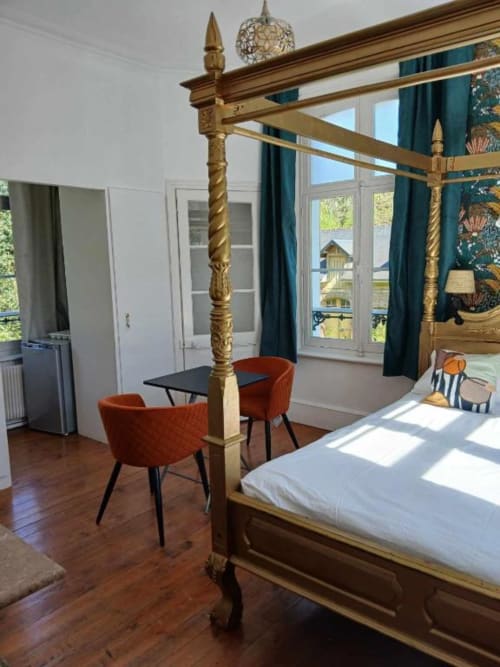 Chambre élégante avec lit à colonnes doré, fauteuils en velours rouge et portes-fenêtres surplombant le repère de Mons-Boubert au