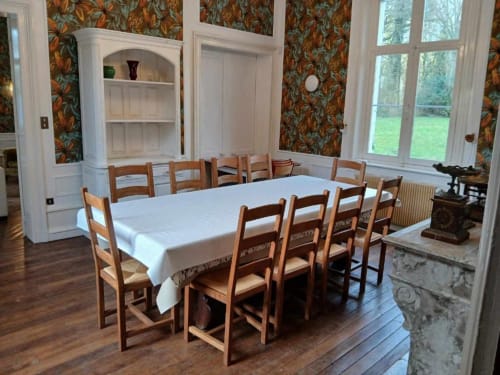 Salle à manger élégante du château de Mons Boubert avec chaises en bois, nappe blanche, papier peint floral et vue sur le jardin