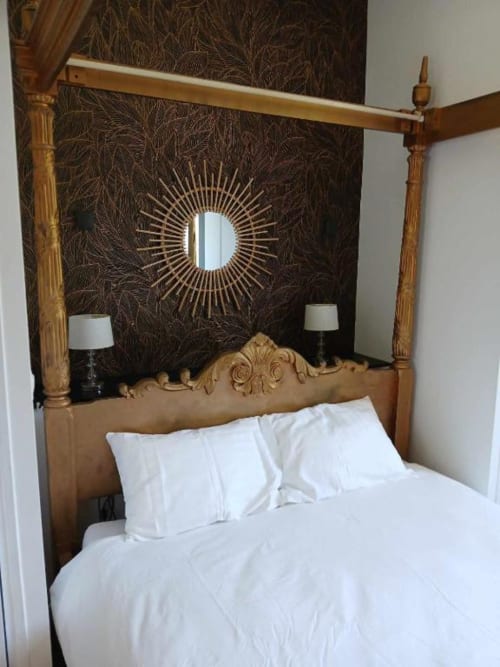 Lit à baldaquin élégant aux draps blancs du château de Mons Boubert, avec tête de lit en bois ornée et motif soleil
