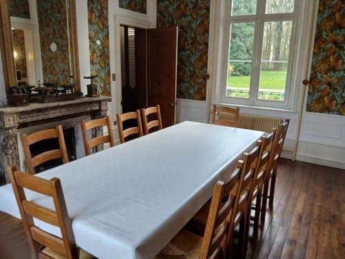 Salle à manger élégante du château de Mons Boubert avec longue table, chaises en bois et vue sur les jardins par les portes-fenêtres