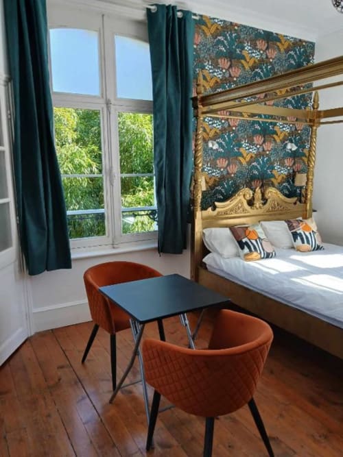 Chambre élégante au château de Mons Boubert avec lit à baldaquin orné, tête de lit floral turquoise, fauteuils velours orange