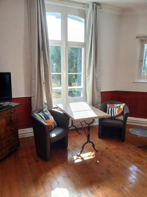 Spacieux séjour du château de Mons Boubert avec parquet, fauteuils noirs, commode en bois et décor français
