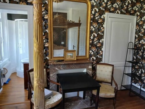 Chambre élégante de villa française avec miroir doré, cheminée, mobilier d'époque et papier peint à motifs floraux sombres au château de