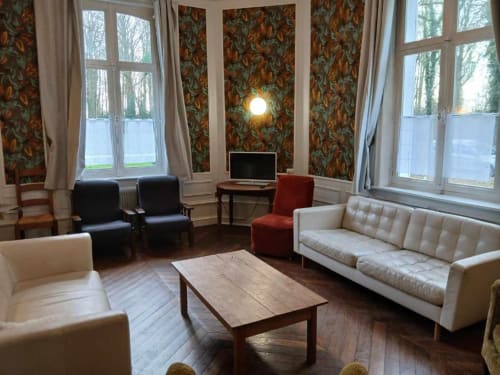 Élégant salon de villa française avec papier peint vintage, canapés crème, cheminée et vue sur le jardin au château de Mons