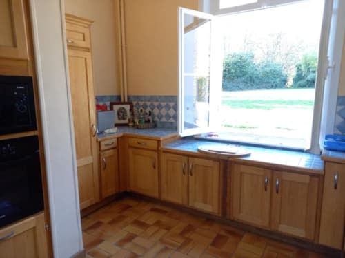 Cuisine lumineuse avec meubles en bois, dosseret en carrelage bleu et vue sur le jardin de la villa Le château de Mons Boubert