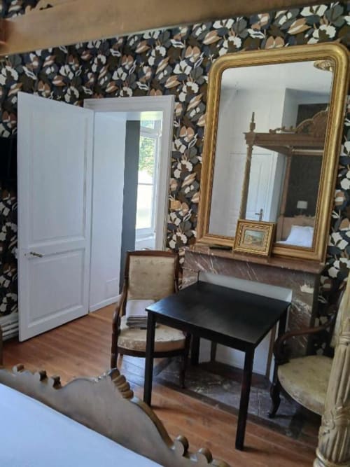 Élégante chambre avec miroir doré, bureau noir, chaise en bois et papier peint floral à la villa Le château de Mons Boubert.