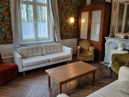 Élégant salon du château de Mons Boubert avec canapé crème, table en bois, cheminée et papier peint floral