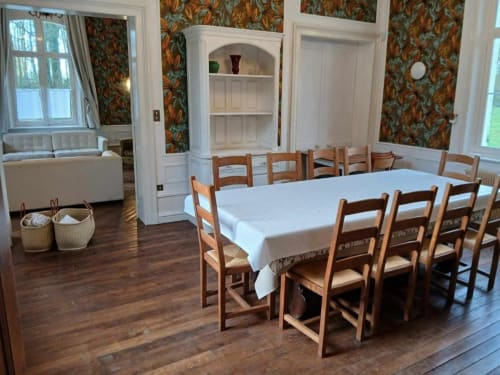 Élégante salle à manger de villa française avec chaises en bois, nappe blanche, papier peint floral et étagères intégrées au Château