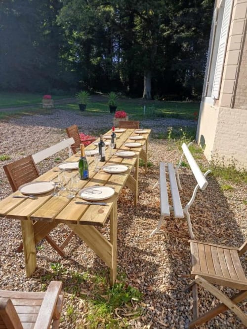 Longues tables de bois pour repas en plein air au château de Mons Boubert, terrasse gravillonnée, pelouse verte et arbres