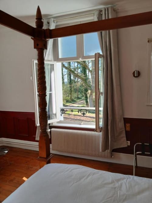 Chambre élégante avec lit à baldaquin en bois offrant une vue sur la forêt au château de Mons Boubert.
