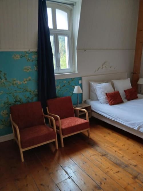 Chambre spacieuse du château de Mons Boubert avec lit, fauteuils rouges, parquet et papier peint turquoise