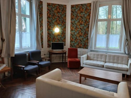 Spacieux séjour du château de Mons Boubert avec canapés crème, fauteuils foncés, papier peint fleuri, parquet