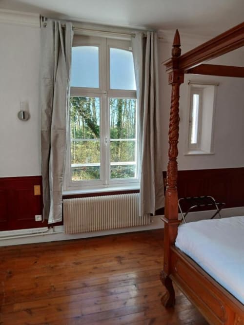 Chambre spacieuse avec lit à quatre colonnes en bois, planchers en bois dur et grandes fenêtres donnant sur la campagne au château de