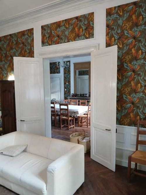 Élégant salon de la villa du château de Mons Boubert avec sièges blancs, papier peint fleuri et accès à la salle à manger