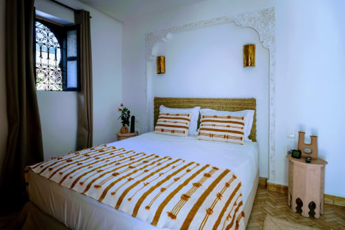 Chambre d'hôtel Dabachi à Marrakech avec literie rayée, appliques dorées et tête de lit en arc ouvragé