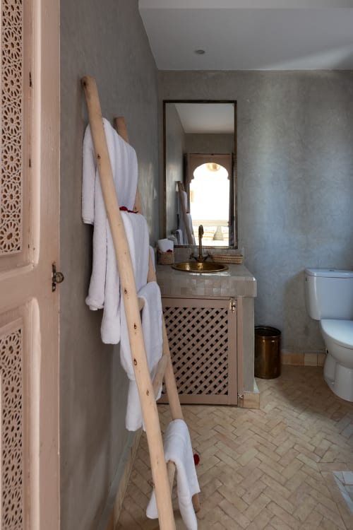 Salle de bains de l'hôtel Dabachi à Marrakech avec échelle à serviettes en bois, miroir, lavabo et toilettes