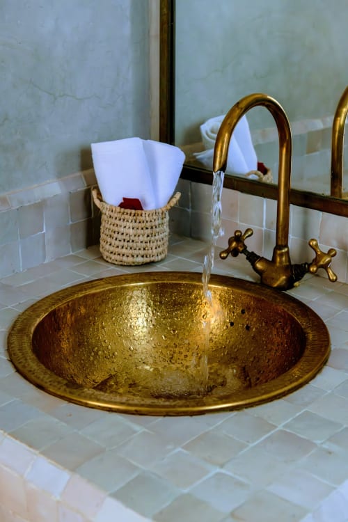 Lavabo en laiton ouvragé avec eau courante et serviettes blanches dans un panier tressé à l'hôtel Dabachi, Marrakech