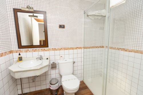 Baño limpio en habitación triple del Hostal Atalaya, Minas de Ríotinto con azulejos blancos, lavamanos, inodoro y ducha