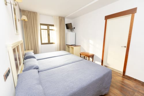 Habitación triple en Hostal Atalaya de Minas de Ríotinto con camas azules, muebles de madera e iluminación natural abundante